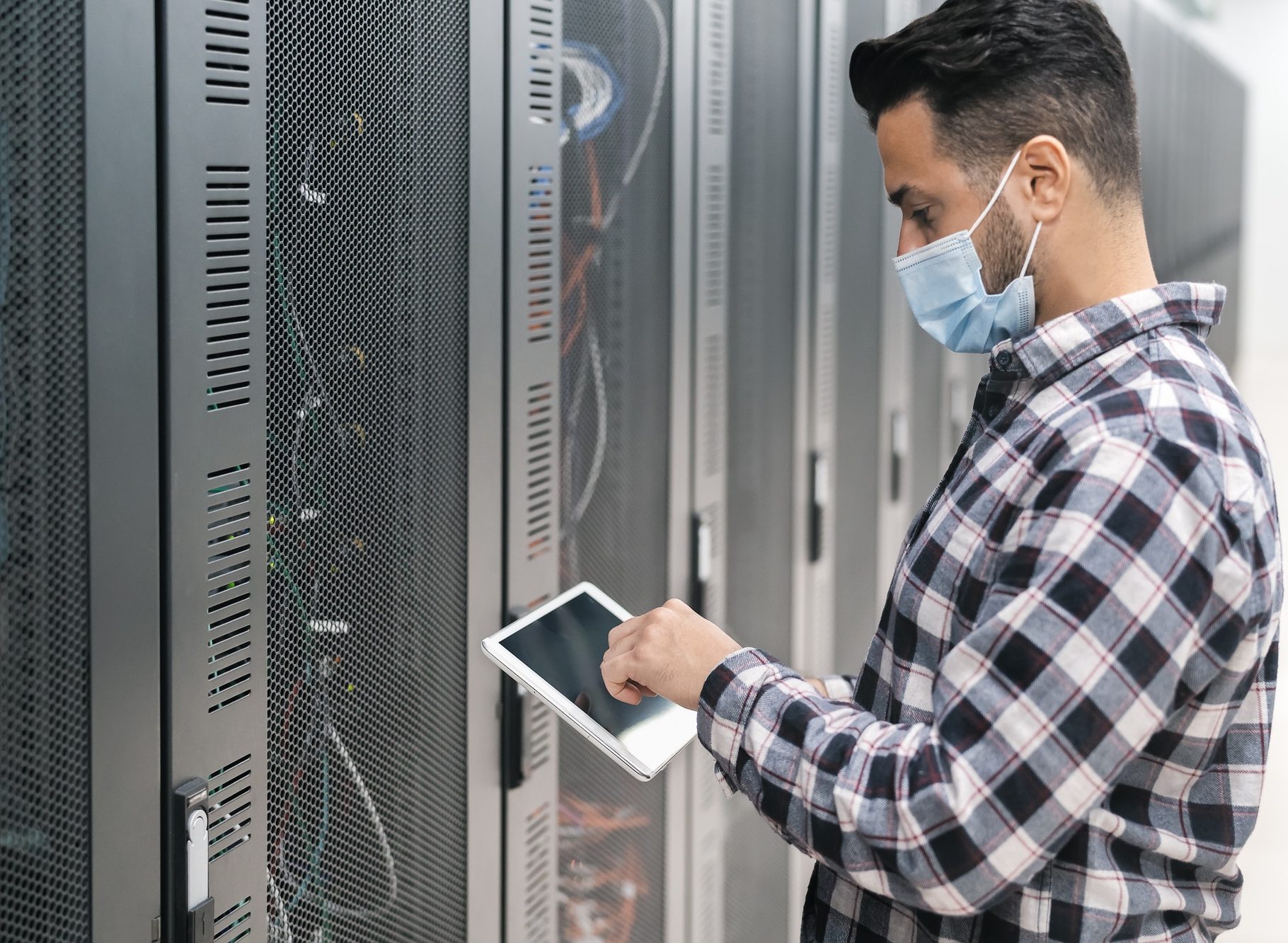 Male informatic engineer working inside server room database while wearing face mask